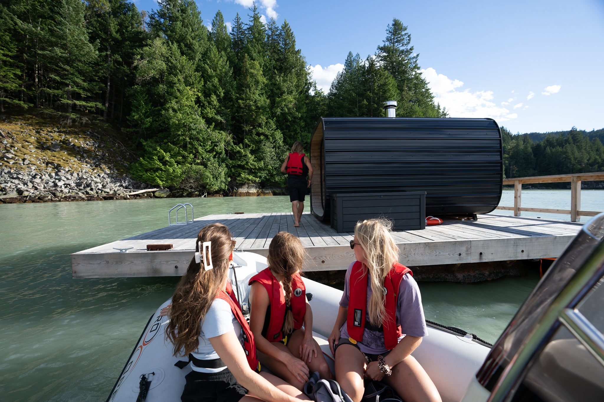People on a boat with a floating sauna in a forested area