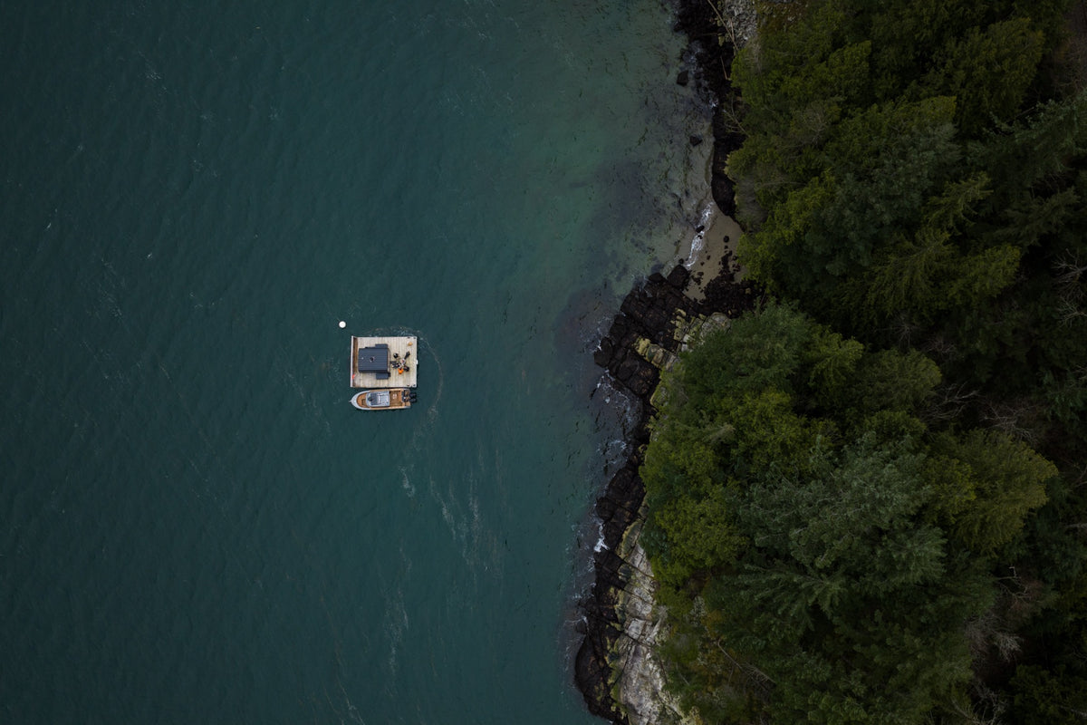 An overhead view of InFlow’s floating sauna beside the forested shoreline